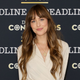 Dakota Johnson, dressed in a white long-sleeved shirt, smiles in front of a Deadline Contenders Award backdrop.